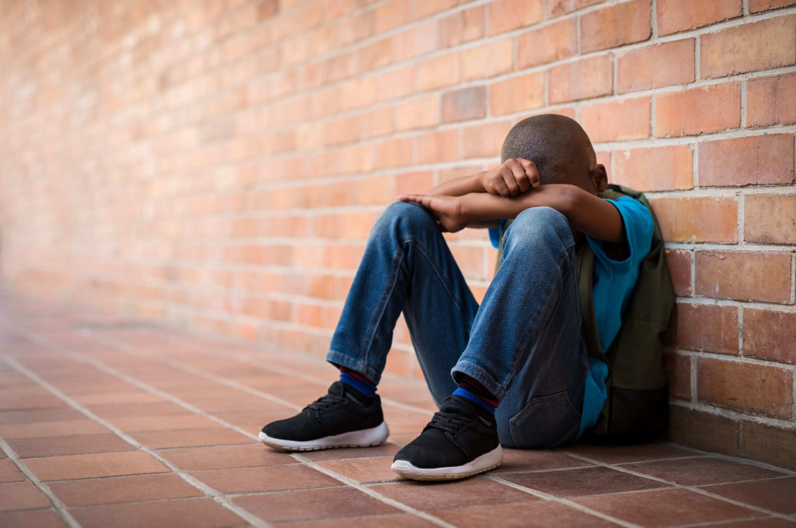 Young boy sitting alone with sad feeling at school. Depressed child abandoned in a corridor and leaning against brick wall. Sexually Abused Trauma