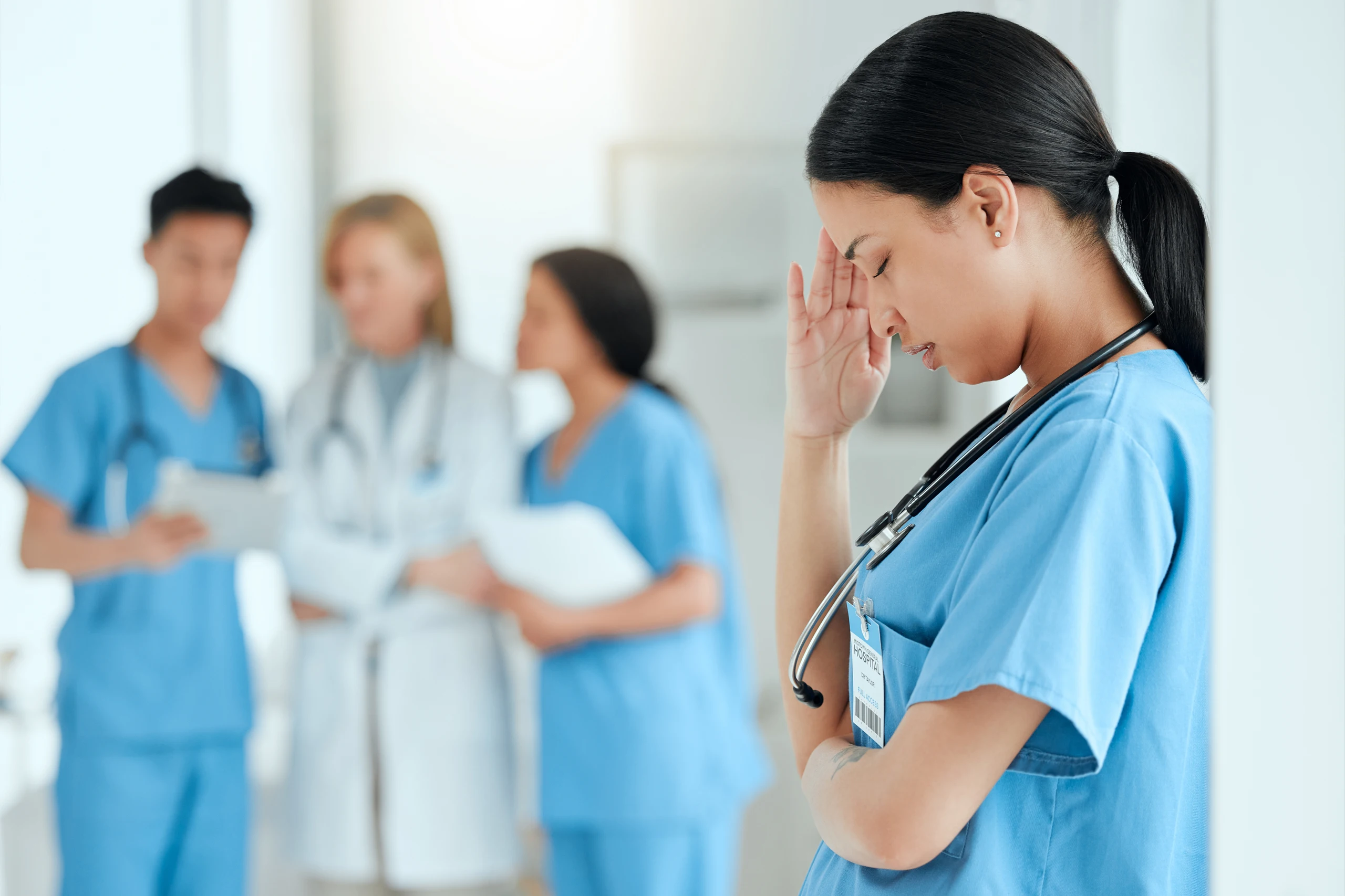 Medical setting with a distraught nurse in the foreground and two nurses and a doctor converse i nthe background